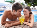 Sharing a drink. an attractive young couple sharing a cocktail on the edge of a pool.