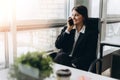 Sharing good business news. Attractive young woman talking on the mobile phone and smiling while sitting at her working place in Royalty Free Stock Photo