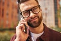 Sharing great news. Close up portrait of happy bearded man in casual wear and eyeglasses talking by phone and smiling