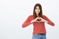 Sharing love and friendliness with friends. Attractive positive female student in casual outfit, showing heart gesture