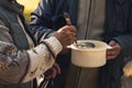 Sharing warm food with people in need concept. Cooking pot full of soup is handled between homeless people who share it