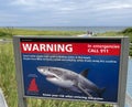Shark attack warning panel in Cape Cod area with beach and tourists on the background