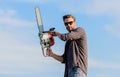 Sharp blade. Handsome man with chainsaw blue sky background. Gardener lumberjack equipment. Lumberjack with chainsaw in Royalty Free Stock Photo