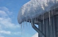 Sharp bright icicles and melted snow hanging from eaves of roof with blue sky in the background