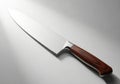 A sharp chef\'s knife with a wooden handle resting on a reflective surface isolated on white background Royalty Free Stock Photo