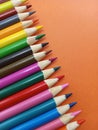 Sharp colorful pencil crayons lined up on an orange background