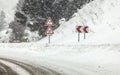 Sharp curve on road, with road signs careful skid, snow during heavy snowstorm blizzard in winter. Dangerous driving conditions
