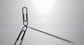 Black paperclip standing upright on a minimalist white surface, casting a long shadow Royalty Free Stock Photo