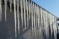 Sharp icicles and melted snow hanging from eaves of roof. Beautiful transparent icicles slowly gliding of a roof