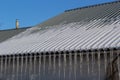 Sharp icicles and melted snow hanging from eaves of roof. Beautiful transparent icicles slowly gliding of a roof