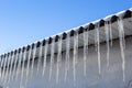 Sharp icicles and melted snow hanging from the eaves of the roof. Beautiful transparent icicles slowly gliding of a roof