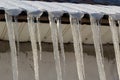 Sharp icicles and melted snow hanging from the eaves of the roof. Beautiful transparent icicles slowly gliding of a roof