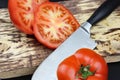 A Sharp knife and a tomato on black background on black surface. Cook on a wooden board slices tomatoes, close-up, macro