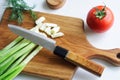 Sharp knife, vintage solid oak wooden cutting board, chopped green onion and fresh tomato on a light background. The concept of Royalty Free Stock Photo