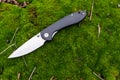 A sharp pocket knife lying on the moss. Knife with a black handle