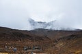 Sharp ridge of Mt Ruapehu peeking through thick fog creeping over desolated lava fields on the slopes of the mountain