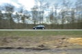The sharp silhouette of the car in motion against the background of a blurred forest. Panoraming. Spring