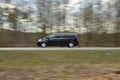 The sharp silhouette of the car in motion against the background of a blurred forest. Panoraming. Spring