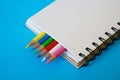 Sharpened colored pencils lie together with a blank notepad on a blue background Royalty Free Stock Photo