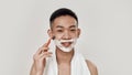 Shave easily. Portrait of shirtless young asian man with towel around his neck shaving his face, looking at camera Royalty Free Stock Photo