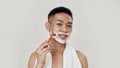 Shave everyday. Portrait of shirtless young asian man with towel around his neck shaving his face, looking at camera Royalty Free Stock Photo