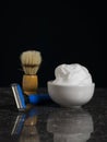 Shaving brush, foam and a man`s razor on a stone table on a black background. Royalty Free Stock Photo