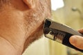 A man shaves his beard with an electric razor in front of a mirror. Care for a man`s beard at home Royalty Free Stock Photo