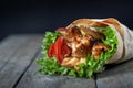 Shawarma rolled in lavash, moist grilled meat with onion, herbs and vegetables on wooden background.