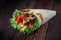 Shawarma rolled in lavash, moist grilled meat with onion, herbs and vegetables on wooden background.