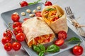 Shawarma sandwich with fresh vegetables and sauce on the gray plate decotated with cherry tomatoes, basil leaves, knife and fork