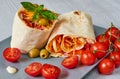 Shawarma sandwich or lavash with fresh vegetables and sauce on the gray plate decotated with cherry tomatoes, basil leaves