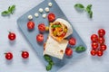 Shawarma sandwich or lavash snack with fresh vegetables on the gray plate decotated with cherry tomatoes, basil leaves, sauce