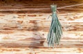 A sheaf of green spikelets hangs on a rope near a log cabin