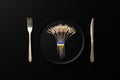 A sheaf of wheat on a black plate tied with the flag of ukraine. golden knife and fork, 3d rendering. concept of hunger and supply