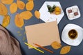 Sheet of brown craft paper, white envelope with note and flower, yellow and orange leaves, color pencils, cup of herbal tea and c