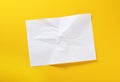 A sheet of crumpled white paper on a yellow background. Crumpled white paper background. Wrinkled leaf texture, top view. Royalty Free Stock Photo