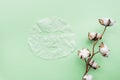 Sheet facial mask and cotton flower on pastel green paper background. Skin care, dermatology, beauty concept. Top view, flat lay,