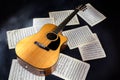 sheet music scores and classical acoustic six-string yellow guitar with black pickguard on isolated black background