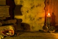 A sheet of old paper with space for text, old yellowed books and scrolls, a burning candle, a compass and a shell stand on the old Royalty Free Stock Photo