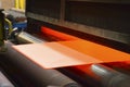 Sheet of orange-coloured material being fed through machine Royalty Free Stock Photo
