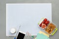 Sheet of paper in small blue cell. Lunchbox with fruits and nuts. Smartphone, colored pencils, bottle of yoghurt, and note paper