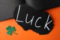 Sheet of paper with word LUCK and clover leaf on orange background