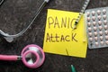 Sheet of paper with words PANIC ATTACK, stethoscope and medicines on dark table