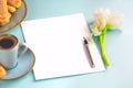 A sheet of white paper is empty on a blue background with an ink pen and a white tulip. Copy space.