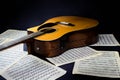 sheets with musical scores and acoustic yellow six-string guitar with black pickguard on isolated black background