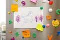 Sheets of paper, child`s drawing and magnets on refrigerator door