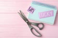 Sheets of paper with word UNLUCKY, notebook and scissors on pink wooden table. Space for text Royalty Free Stock Photo