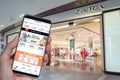 shein app on a smartphone screen in front of a Zara store entrance.