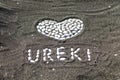 Shell heart on a seaside beach on black magnetic sand with the inscription Ureki. Royalty Free Stock Photo