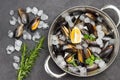 Shellfish mussels in shells in saucepan with lemon and ice. Rosemary, ice and raw mussels on table